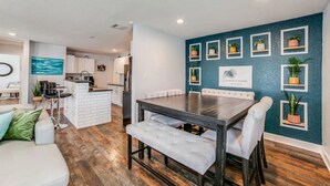 Una cocina moderna con armarios blancos, una isla central y una zona de comedor con una mesa de madera oscura y sillas tapizadas en blanco.