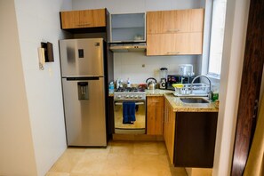 A compact kitchen with a stainless steel refrigerator, a built-in oven, a gas stove, and wooden cabinets.