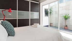 Ein Schlafzimmer mit einem großen Bett, einer roten Schreibtischlampe und Blick nach draußen durch eine Glastür.