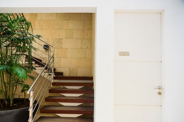 A staircase with a metal railing leading to a beige wall, a white door with a lock, and a potted plant on the left.