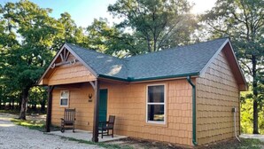 A small wooden cabin with a sloped roof, a front porch with a bench, and a gravel driveway. - Antler Ridge Cabin #4 (Sulphur)