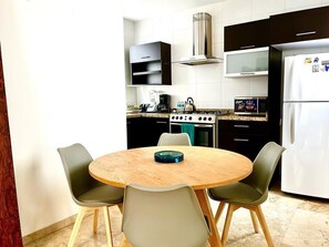 A modern kitchen with a round wooden table, four chairs, a stove, a microwave, and a refrigerator.