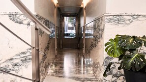 A marble-floored hallway with a metal railing, a potted plant, and a door at the end.