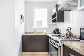 A modern kitchen with dark cabinetry, a gas stove, a kettle, and a window providing natural light.