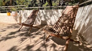 Two wooden lounge chairs with metal frames, positioned on a concrete surface with a metal railing in the background.