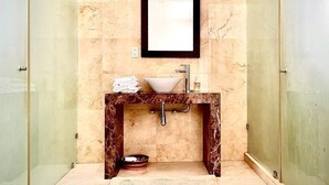 A bathroom with a marble vanity, a sink, a mirror, and a shower enclosure. - Condesa Residence Amsterdam G (CDMX)