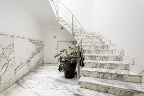 A marble staircase with a metal handrail, a potted plant, and a door with a letter 'C' sign.