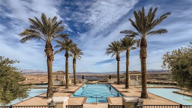 Zona de piscina con palmeras, cielo despejado y montañas a lo lejos.