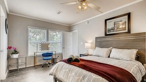 Une chambre à coucher comprenant un lit, un bureau, une chaise, un ventilateur de plafond et une fenêtre avec des stores.
