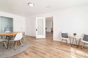 A modern interior with a wooden dining table, white chairs, a patterned rug, and a white door leading to another room.