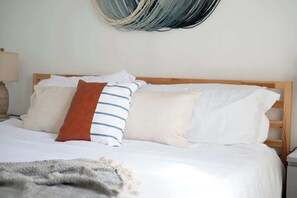 A bed with white bedding, a brown and blue striped pillow, and a gray throw blanket.