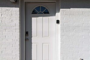 A white door with a small window above it, set in a white brick wall.