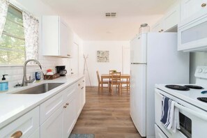 Una cocina compacta con armarios blancos, un lavamanos, una estufa y un comedor con mesa y sillas.