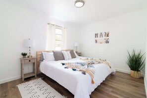 Un dormitorio con cama, mesitas de noche, una ventana con cortinas y decoración en la pared.