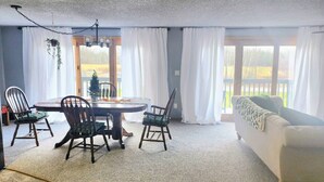Ein Essbereich mit einem runden Tisch, vier Stühlen, einer Couch und Blick auf eine Terrasse durch große Fenster.
