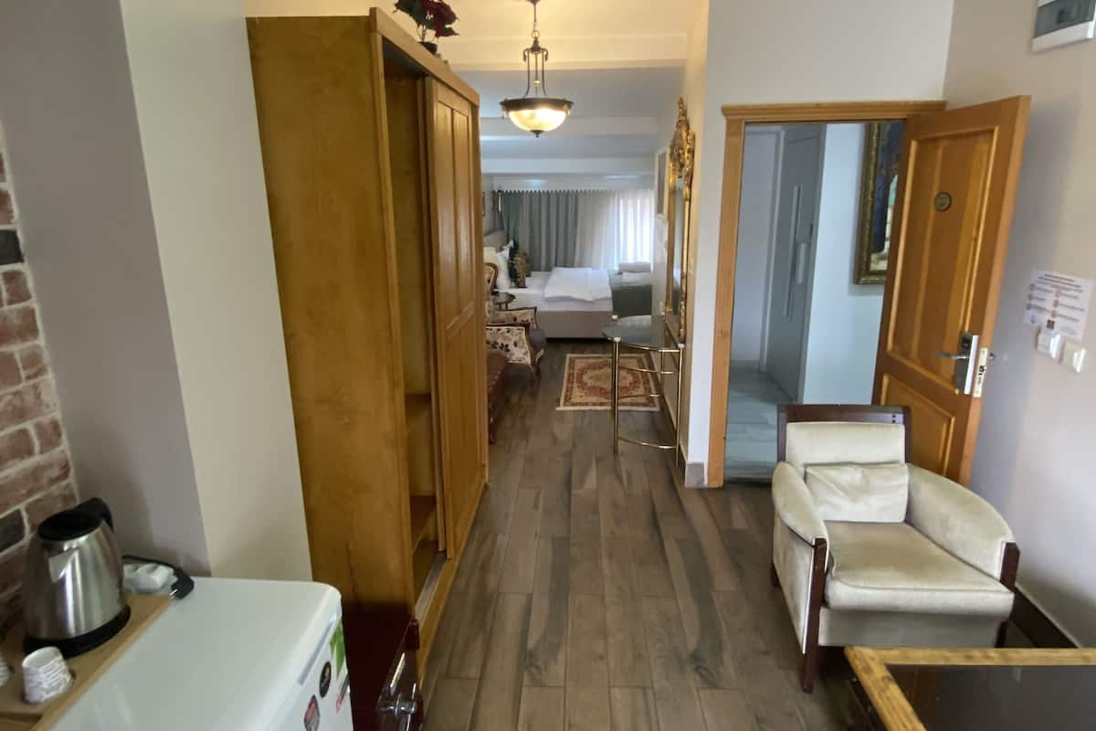 A narrow hallway with a wooden wardrobe, a white refrigerator, and a beige armchair. A dining table is visible in the distance.