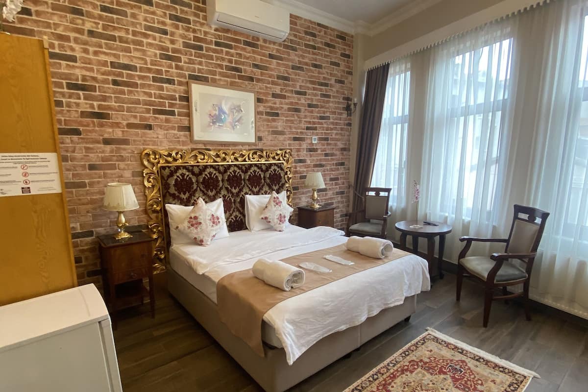 A hotel room with a brick wall, a chandelier, a bed with white linens, a wooden floor, a small round table, and a chair.