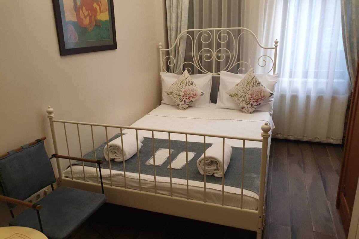 A neatly made bed with pillows and a folded towel, a chair, and a painting on the wall.