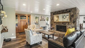 A living room with a stone fireplace, a sofa, a patterned armchair, and a coffee table. - Spacious home near old mill w/pool table & hot tub (Bend)