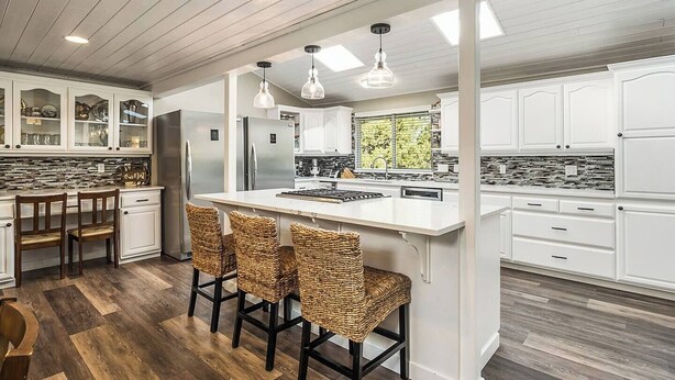 A modern kitchen with white cabinetry, a central island with bar stools, and pendant lighting. - Spacious home near old mill w/pool table & hot tub (Bend)