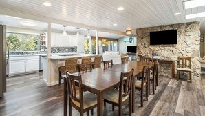 A spacious kitchen with white cabinets, a large island, and a dining area with a stone accent wall and a flat-screen TV. - Spacious home near old mill w/pool table & hot tub (Bend)