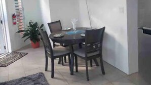 Ein Essbereich mit einem runden Tisch, vier Stühlen, einer Zimmerpflanze und einem an der Wand befestigten Fernseher.