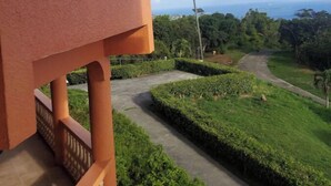 Blick auf ein Gebäude mit einem Balkon, der auf einen angelegten Garten und eine Straße zum Meer blickt.