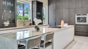 A modern kitchen with a central island, dark cabinetry, and a view of greenery outside. - On The Bay With Hot Tub, Pool, Kayaks And More (Hollywood)