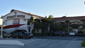 Um hotel chamado "Dynasty Suites" com uma placa de identificação, um estacionamento com vários carros e um céu claro.