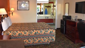Quarto de hotel com cama, escrivaninha, cômoda, televisão e banheiro visível por uma porta aberta.