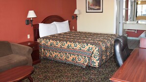 Quarto de hotel com cama, sofá, escrivaninha e banheiro visível por uma porta aberta.