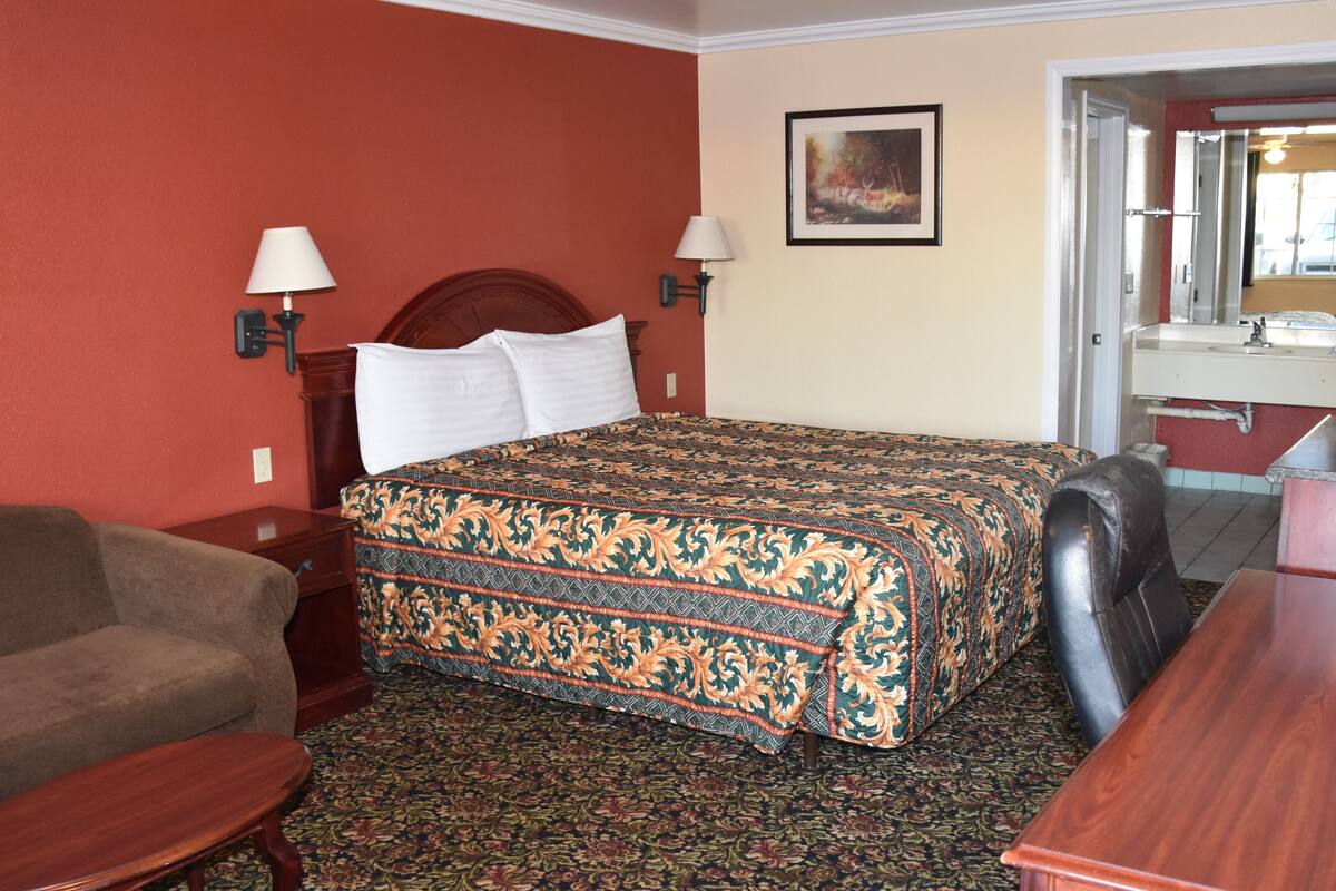 Hotelkamer met een bed, een bank, een bureau en een badkamer zichtbaar door een geopende deur.