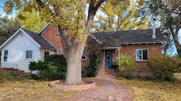 A two-story house with a brick exterior, a front porch, and a large tree in the yard.