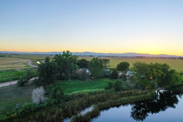 Un paisaje rural con una casa rodeada de campos y un pequeño cuerpo de agua.