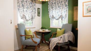A room with two checkered chairs, a small round table with a cup and saucer, and floral curtains.
