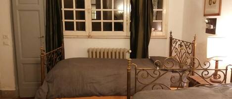 Una habitación con dos camas, un radiador, una ventana con cortinas y una puerta.