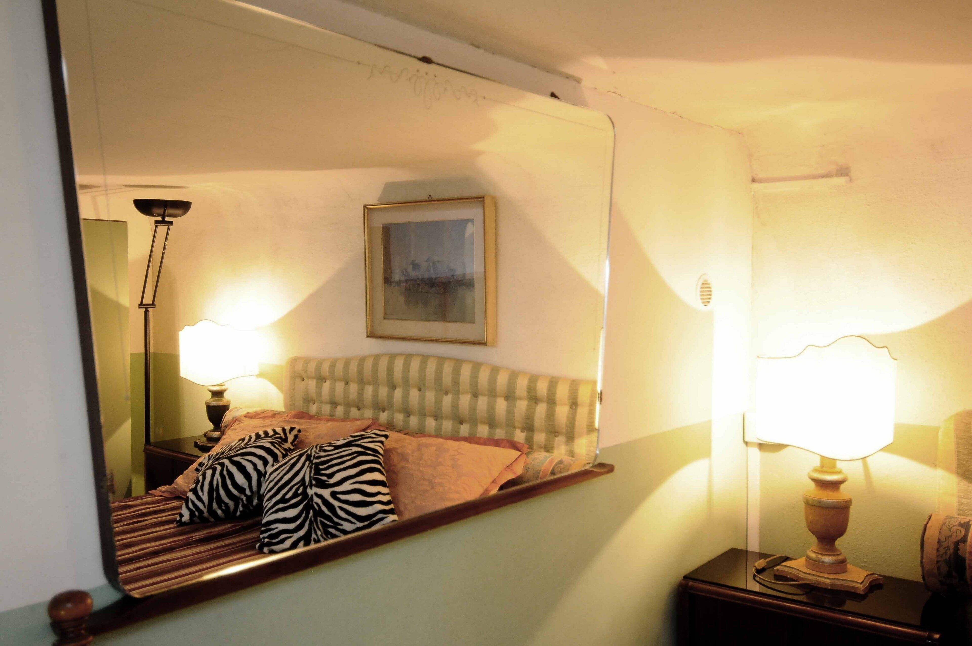 A bedroom with a bed, a headboard, a bedside lamp, a nightstand, and a mirror.