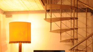 Una escalera con barandilla de metal, un televisor sobre una mesita y una lámpara de pie.