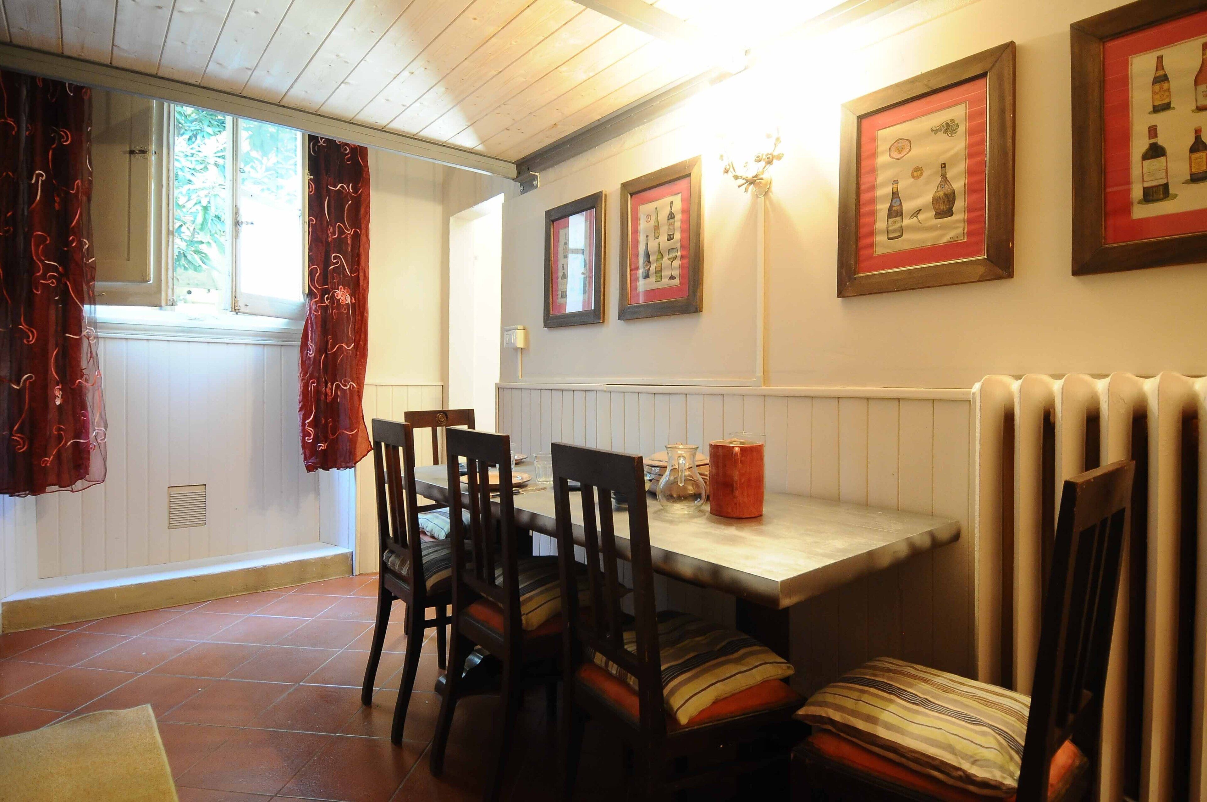 A dining area with a table and chairs, framed pictures on the wall, and a window with curtains.