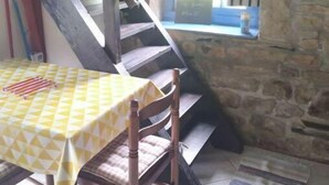 A rustic room with a wooden staircase, a table with a yellow checkered tablecloth, and a stone wall. - The bakery lives in the countryside near hiking trails (Val-Couesnon)