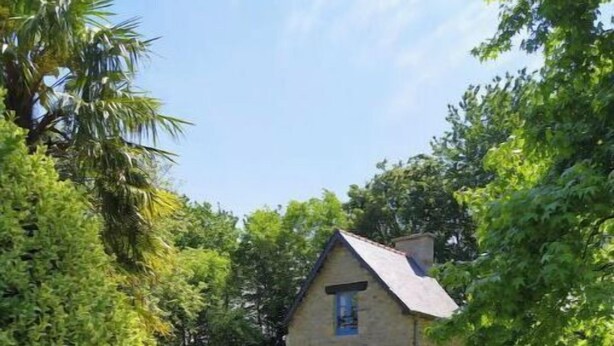 A stone cottage with a sloped roof, surrounded by lush greenery and a well-maintained lawn. - The bakery lives in the countryside near hiking trails (Val-Couesnon)