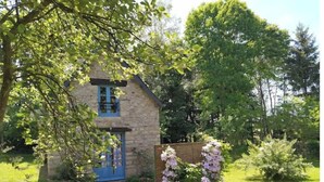 A stone cottage with a blue door and window, surrounded by lush greenery and a gravel path. - The bakery lives in the countryside near hiking trails (Val-Couesnon)