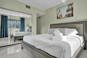 Ein modernes Hotelzimmer mit einem großen Bett, einer Glasabtrennung und einem Palmen-Gemälde.