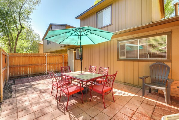 Une terrasse avec une table et des chaises, un parasol vert et une clôture en bois.