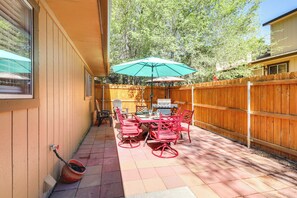 Une terrasse extérieure avec une clôture en bois, une table avec des chaises et un parasol vert.