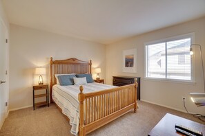 Une chambre avec un lit en bois, deux tables de chevet avec des lampes, une petite table de nuit, une commode, une fenêtre avec des stores et un tableau encadré au mur.