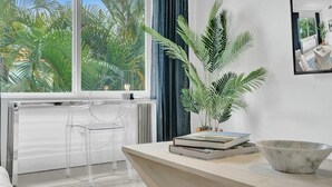 Ein modernes Wohnzimmer mit großem Fenster, einem klaren Sessel, einer Pflanze, einer Marmorschale und einem Bücherstapel.