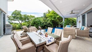 An outdoor patio with wicker furniture, a glass table, and a ceiling fan. - Amigos de Tortuga • 4 BR Villa • Private Pool • Oceanview (Playa Hermosa)