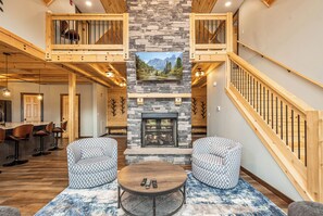 A spacious living area with a stone fireplace, wooden ceiling, and a mezzanine level. - Sunshine Chalet by Taylor Made Deep Creek (McHenry)