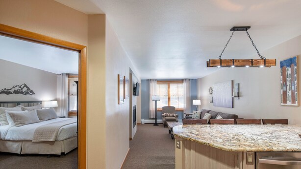 A hotel room with a bed, a desk, a chair, a kitchen area with a countertop, and a dining table. - Premium Unit 1108 - One Bedroom - Zephyr Mountain Lodge 1 Condo (Winter Park)
